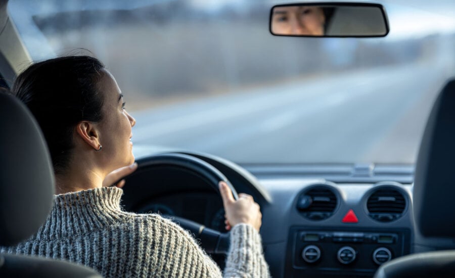 A woman driving on an Alberta highway, wondering why auto insurance is so expensive in the province.