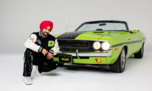 Diljit-Dosanjh wears a Simplii Financial jacket while posing with a car