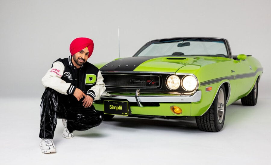 Diljit-Dosanjh wears a Simplii Financial jacket while posing with a car