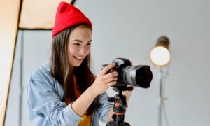 A smiling young woman holds a camera in a studio