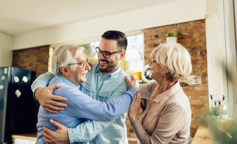 Happy senior parents and their adult son having fun while greeting in the kitchen.