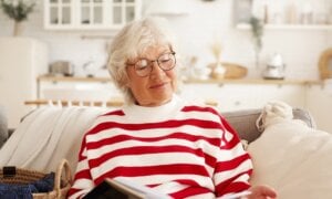 A retired woman on a sofa reading a book