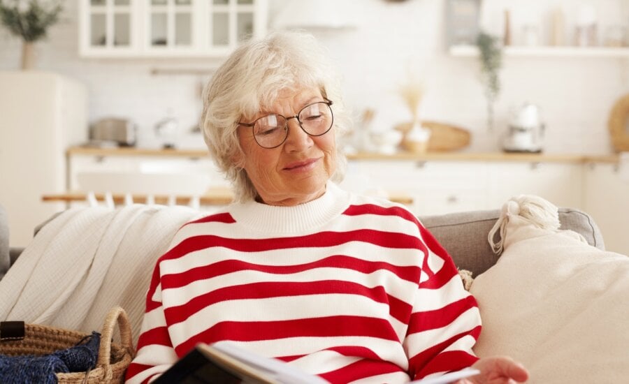 A retired woman on a sofa reading a book
