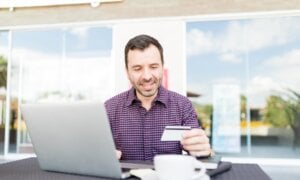 Mid adult man using online banking service to transfer money between accounts using laptop in shopping mall