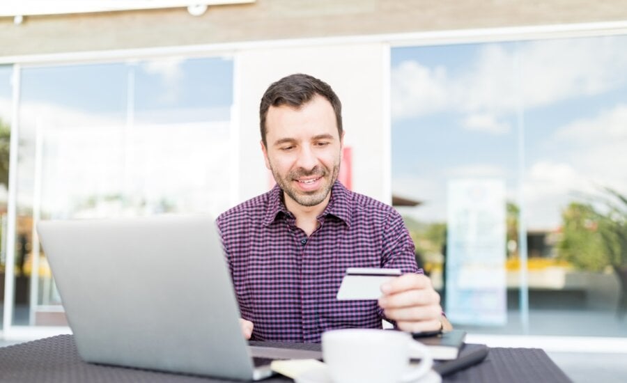 Mid adult man using online banking service to transfer money between accounts using laptop in shopping mall