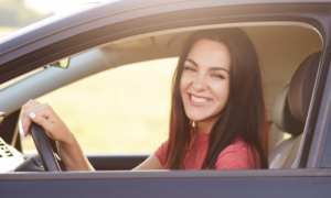 A smiling young woman drives a car