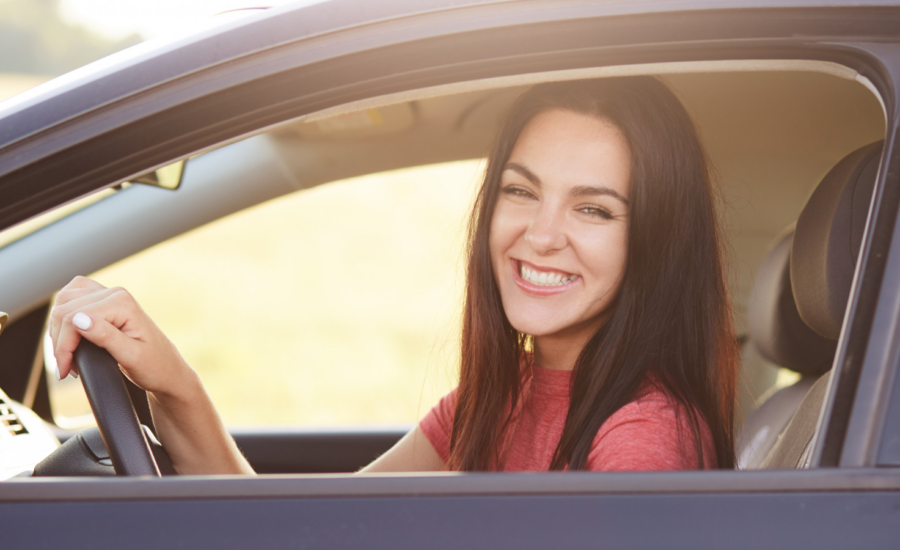 A smiling young woman drives a car