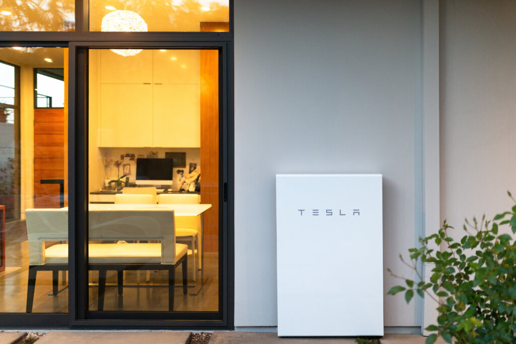 A white rectangular Tesla powerwall on the exterior wall of a house