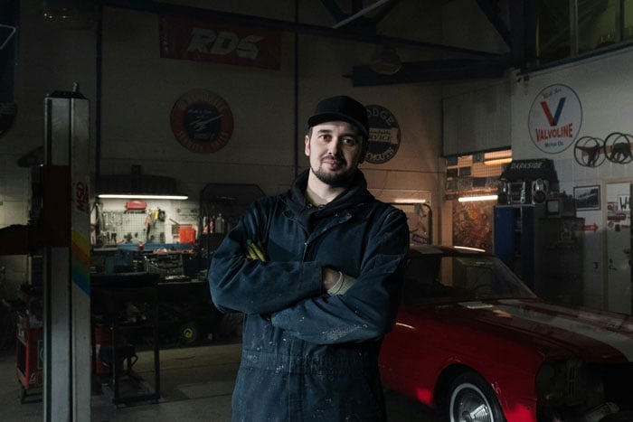 A young man stands in a car repair shop