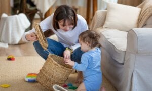 A woman kneels on the floor, looking into an empty basket with her child.