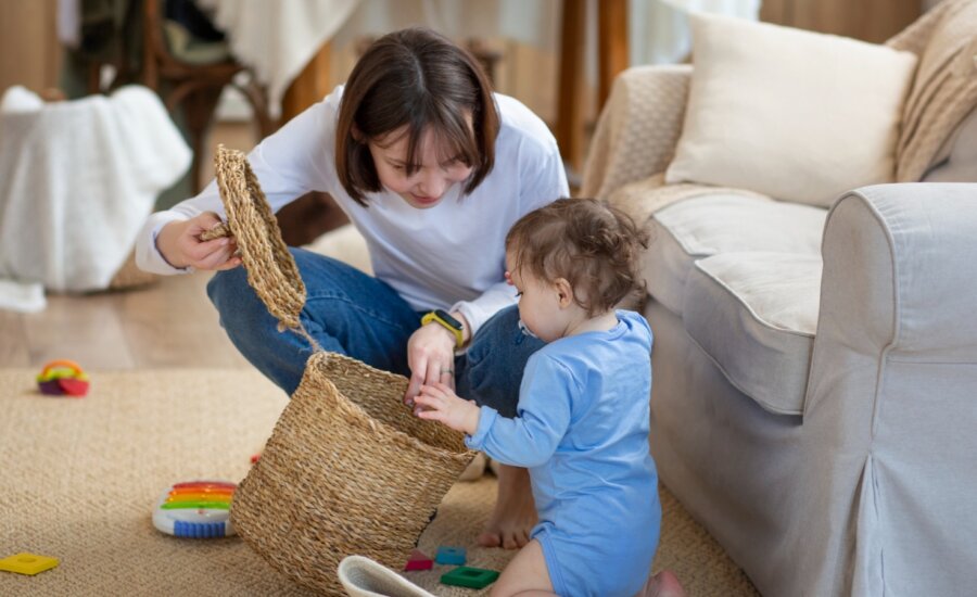 A woman kneels on the floor, looking into an empty basket with her child.