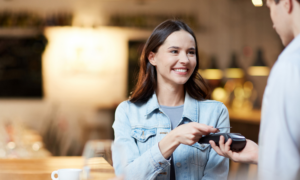 A woman taps her Wise card on a payment terminal to pay for her coffee