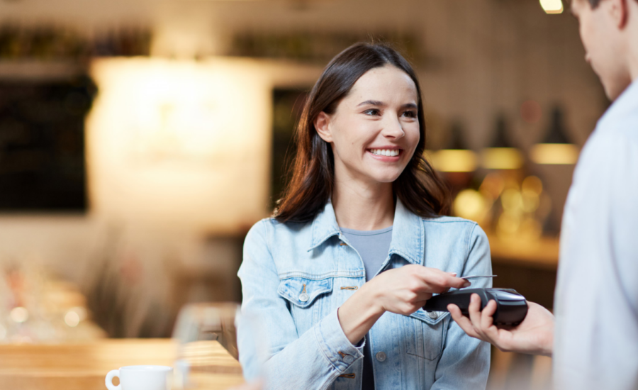 A woman taps her Wise card on a payment terminal to pay for her coffee