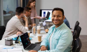 A smiling young computer developer with three of his colleagues in a boardroom.