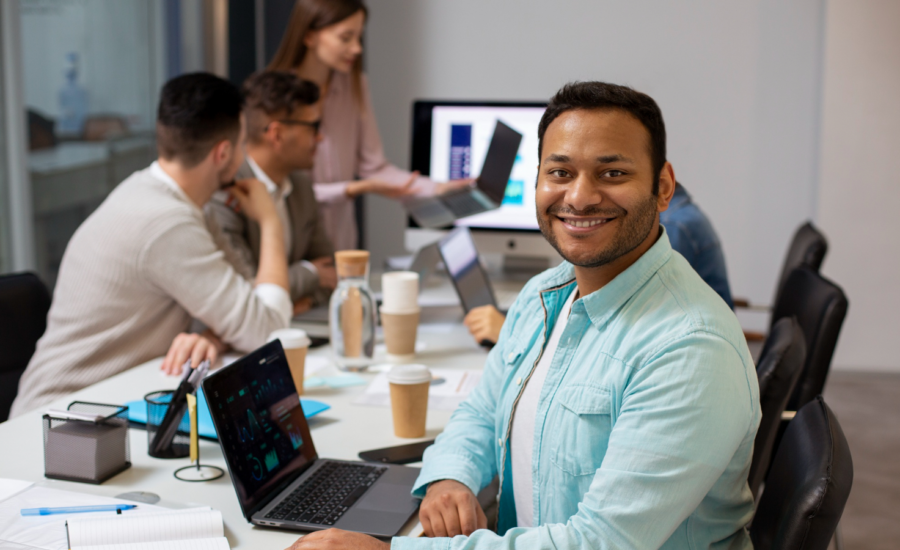 A smiling young computer developer with three of his colleagues in a boardroom.