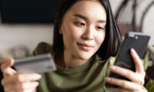 A young woman looks at her phone and holds a credit card