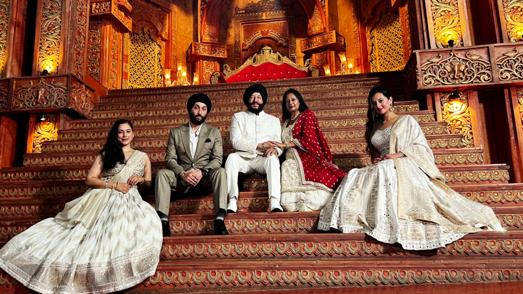 The Singh family sits on an ornate staircase, wearing beautiful Indian clothes