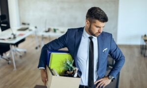 Distraught businessman holding his belongings and feeling worried while getting fired from his job.