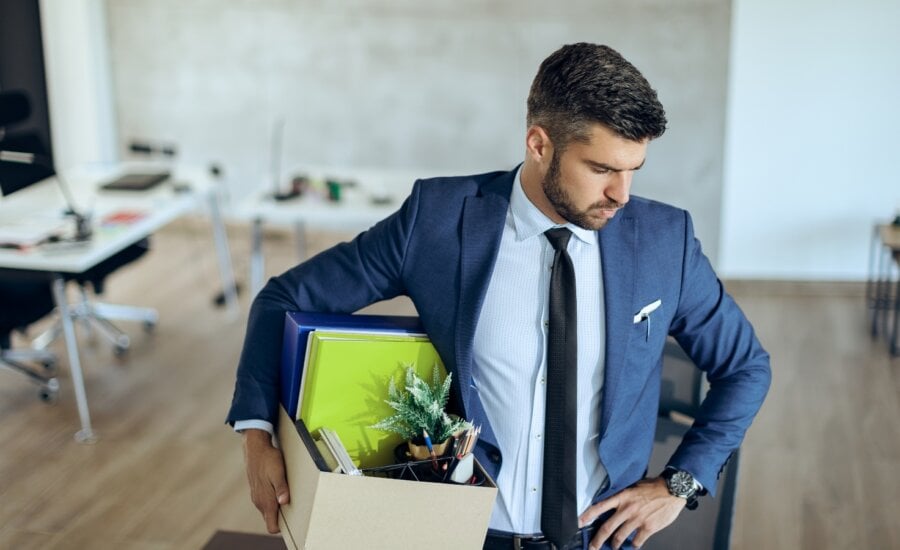 Distraught businessman holding his belongings and feeling worried while getting fired from his job.