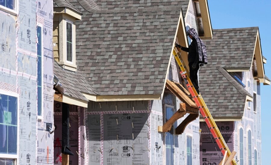 A worker on a ladder works on the exterior of a new home under construction.