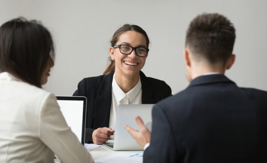 Smiling female CEO wearing glasses talking with company subordinates, discussing business strategies. Colleagues negotiating in positive atmosphere, working at laptops. Cooperation, leadership concept