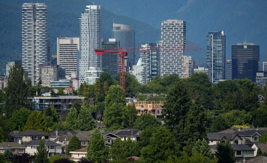 A crane is seen above a wood-frame condo project under construction as condo and office towers line the downtown skyline, in Vancouver, on Friday, July 4, 2025. While optimism is building in some parts of Canada for a second-half rebound in the real estate market, condominium dwellers aiming to move up to a larger space face tough choices amid little sign of improvement for that segment.