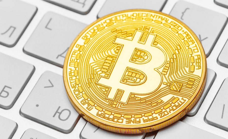A gold bitcoin sits on a computer keyboard