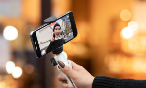 A young woman shoots a video with a selfie stick.