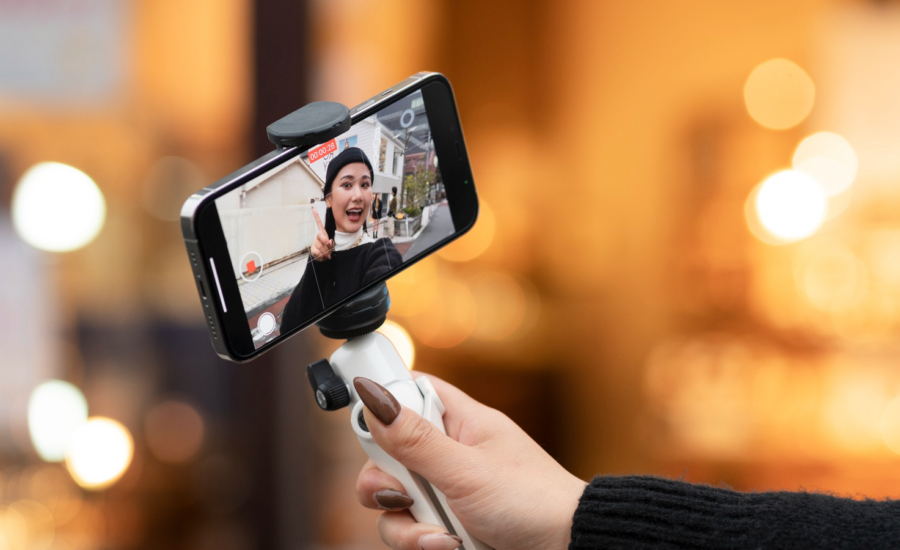 A young woman shoots a video with a selfie stick.