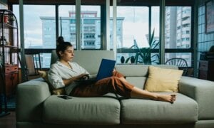 A woman works on her laptop while sitting on a couch