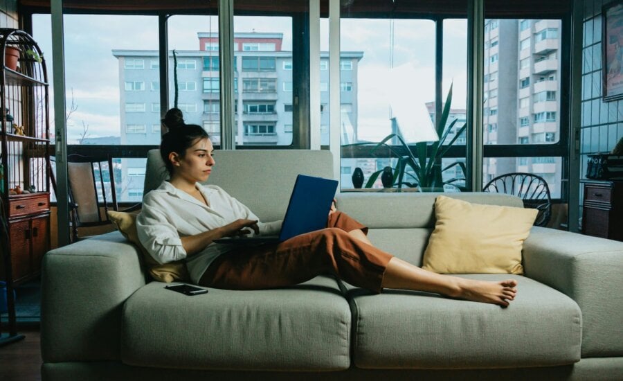 A woman works on her laptop while sitting on a couch