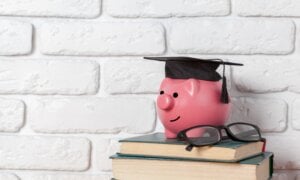 Pink piggy bank with a graduate's cap, sitting on a stack of books