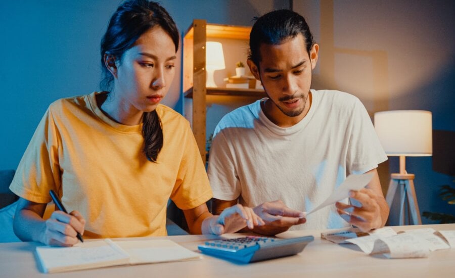 A young couple sits at a desk using a calculator while budgeting