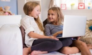Two young girls on a couch using a laptop