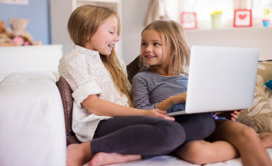 Two young girls on a couch using a laptop