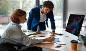 Man and woman discussing stocks at a desk.