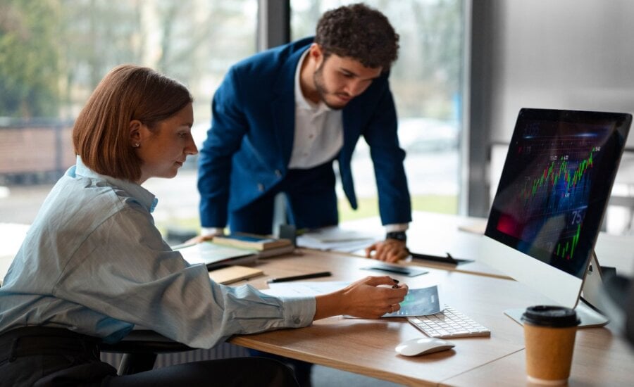 Man and woman discussing stocks at a desk.