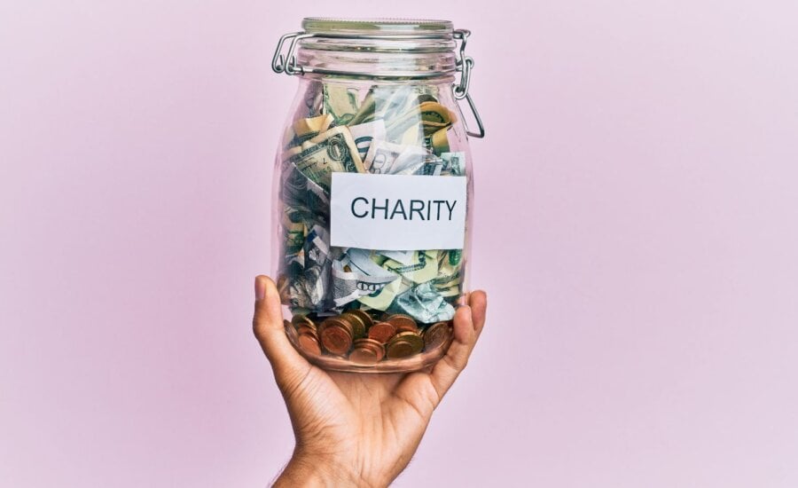 Hand of hispanic man holding charity jar with dollars over isolated pink background.