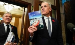 Prime Minister Mark Carney holds up a copy of the budget as he and Minister of Finance and National Revenue Francois-Philippe Champagne make their way to the House of Commons for the tabling of the federal budget on Parliament Hill in Ottawa, on Tuesday, Nov. 4, 2025.