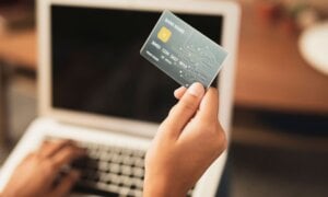 Person holding a credit card in front of a laptop