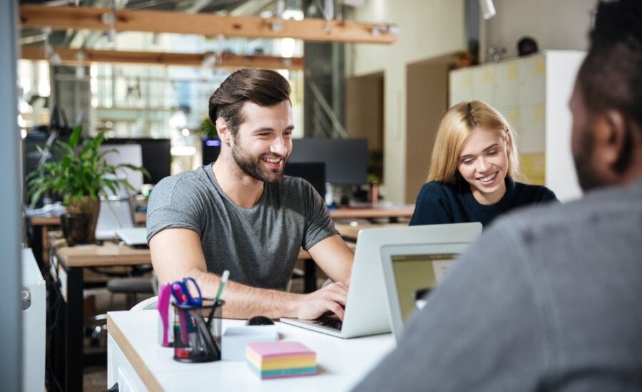 Young people working at a desk with laptops.