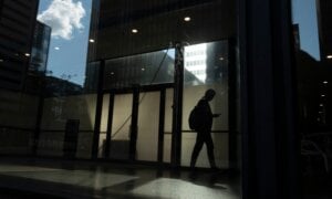 A man walks though a downtown Toronto office building with other buildings reflected in a window in this June 11, 2019 photo.