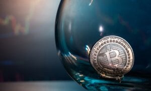 Close-up of a silver Bitcoin on a blue reflective surface in a glass and the histogram of currency in the background.