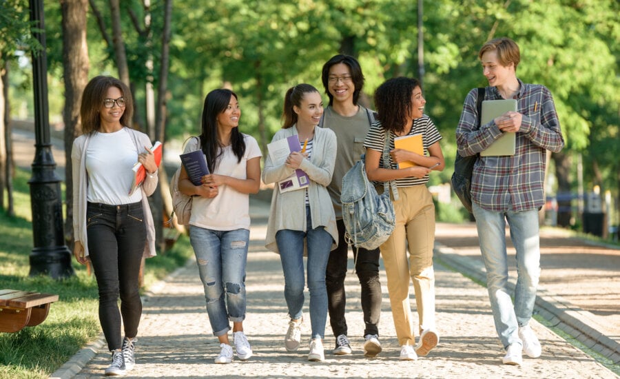 Picture of multiethnic group of young cheerful students walking while talking. Looking aside.