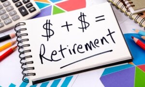 Simple retirement formula written on a notepad surrounded by graphs, charts, calculator, books and pencils.
