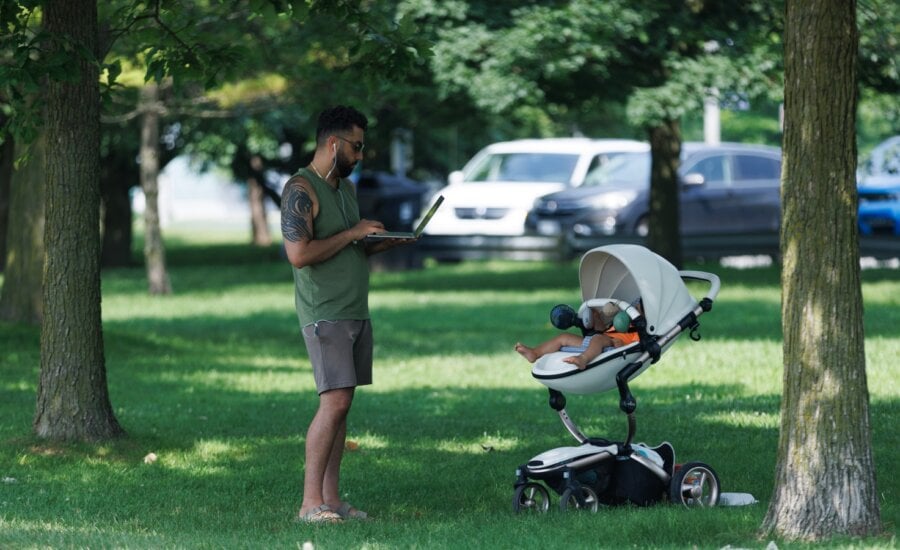 A man is seen on his laptop in the park while a baby naps, in the park on the Toronto waterfront, Thursday July 6, 2023.