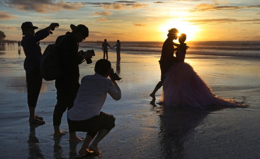 In this Jan. 18, 2017, file photo, photographers take photos of a tourist couple's wedding at the famous Kuta beach during sunset in Bali, Indonesia. (