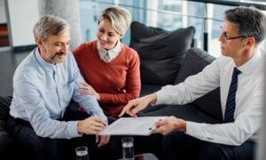Happy man signing an agreement while being on a meeting with insurance agent with his wife.