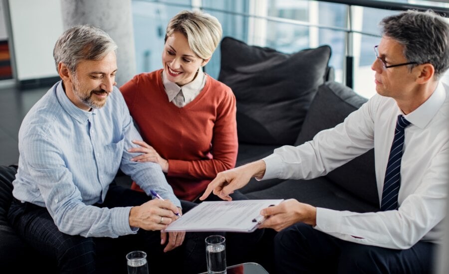 Happy man signing an agreement while being on a meeting with insurance agent with his wife.