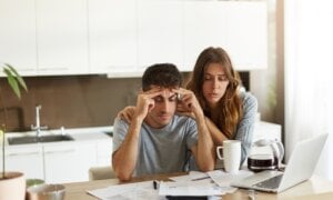 People, relationships, debts, financial stress and economic crisis. Unemployed young Caucasian man feeling depressed, sitting at kitchen table over unpaid bills while his wife trying to cheer him up